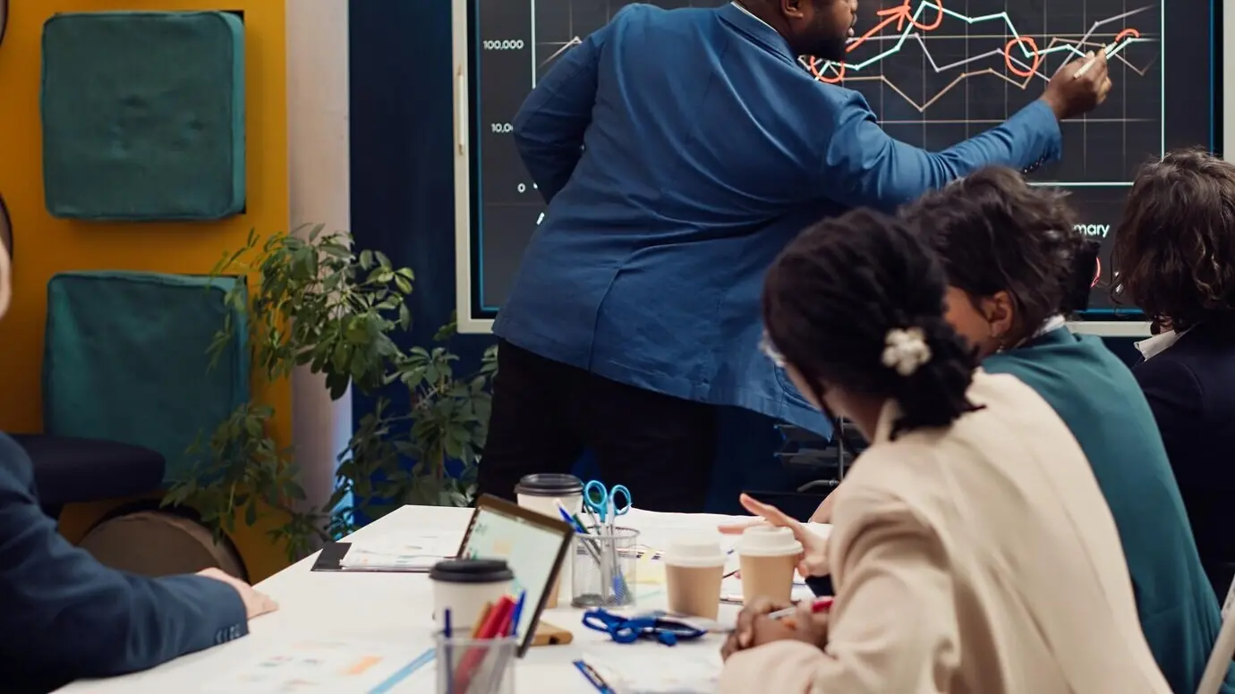 Diversos colegas revisando infografías de ventas mensuales en una pizarra interactiva